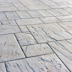 A close-up view of a stone-patterned concrete surface with rectangular and square tiles arranged in a staggered layout, featuring textured, slightly weathered details.