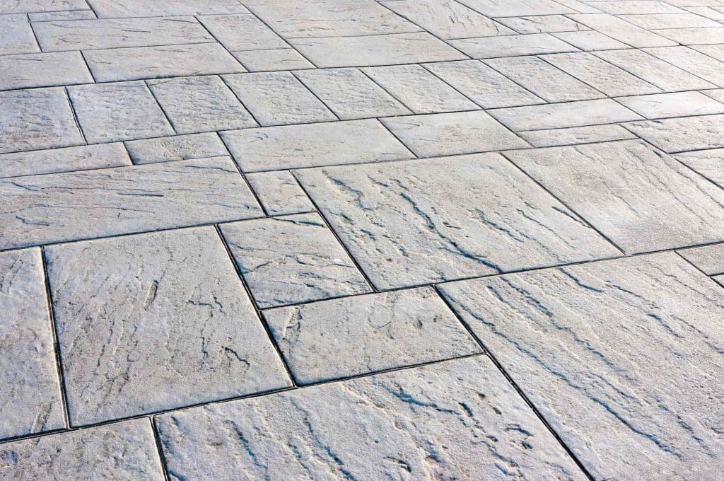 Close-up view of a patterned concrete surface with large rectangular and square tiles, textured to resemble natural stone in light gray tones.
